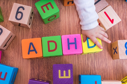 vaikiški raidžių kubeliai, sudėti taip, kad sudarytų pavadinimą ADHD, su vaiko ranka.