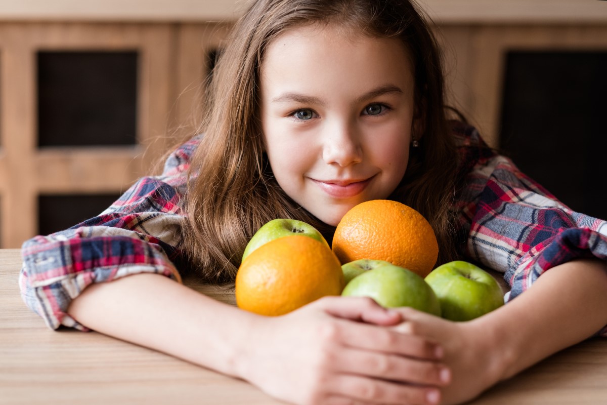 Vaisiuose esantis vitaminas C, vaikas su apelsinais ir obuoliais rankose