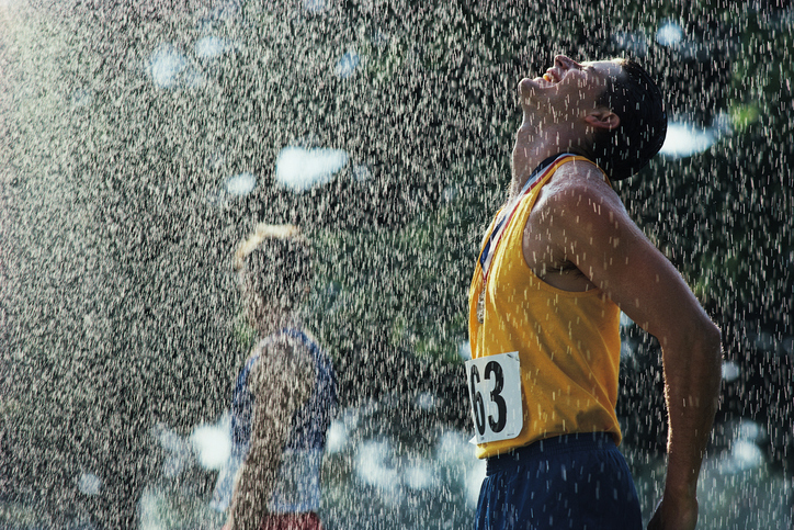 Sportininkas vyras, kirtęs finišo liniją. Lyja lietus. Jo galva pasukta į viršų nuo krintančių lašų. Akys užmerktos, ant kaklo kabo medalis. Jis vilki geltoną liemenėlę su numeriu 63 ir mėlynus šortus.